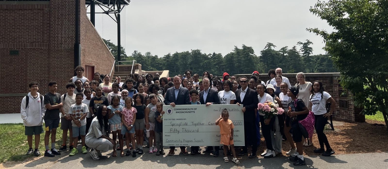 Campers, camp staff and members of the Springfield legislative delegation holding an oversized Commonwealth of Massachusetts check for fifty thousand dollars made out to Springfield Together Camp.